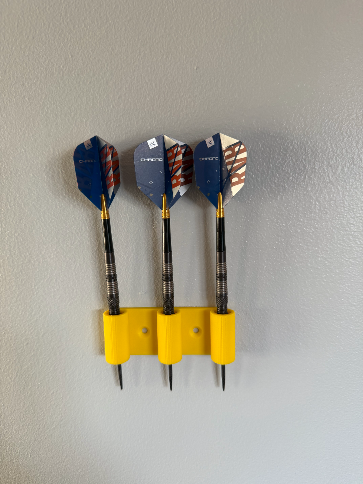 Dartboard Setup at Home: Height, Distance and Storage 1 Three assembled darts stored in a yellow wall-mounted Layered Works holder